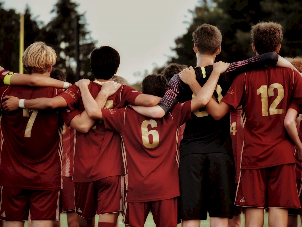 A group of soccer players wearing red uniforms, with their arms around each other, forming a huddle on the field.